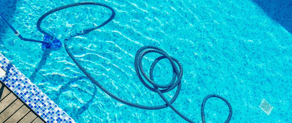 A blue vacuum cleaning the bottom of a pool with blue and white tiles in Bridgehampton, NY.