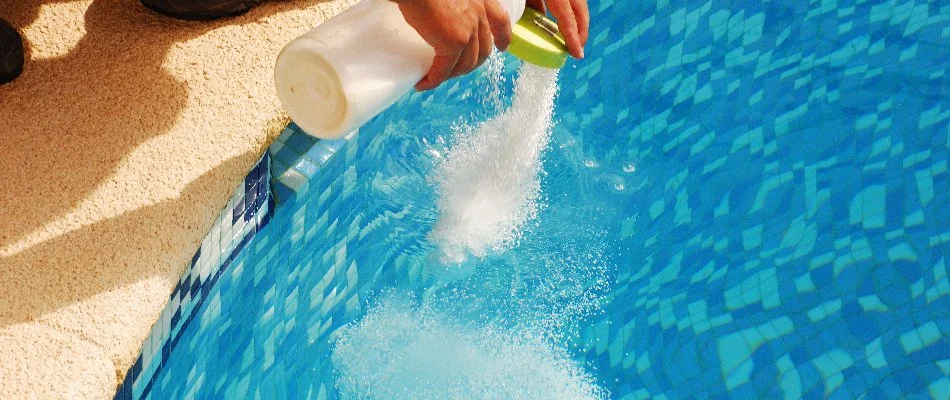 Person adding chemicals to a pool in Bridgehampton, NY.
