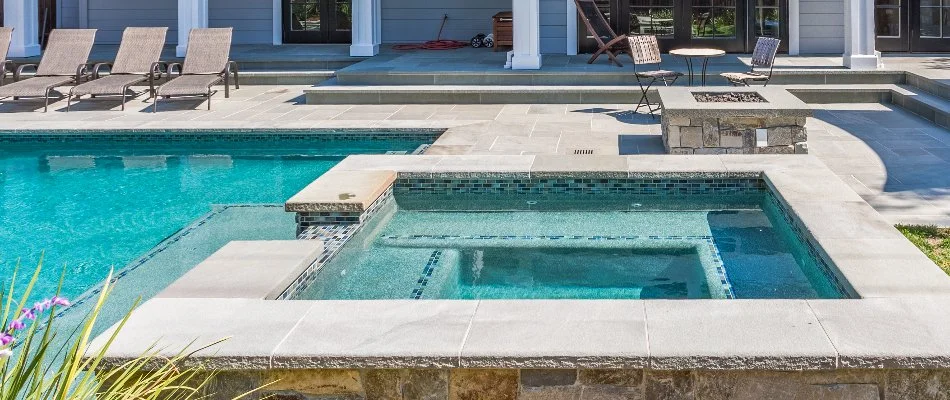 Pool in Bridgehampton, NY, with spa near a fire pit and some chairs.